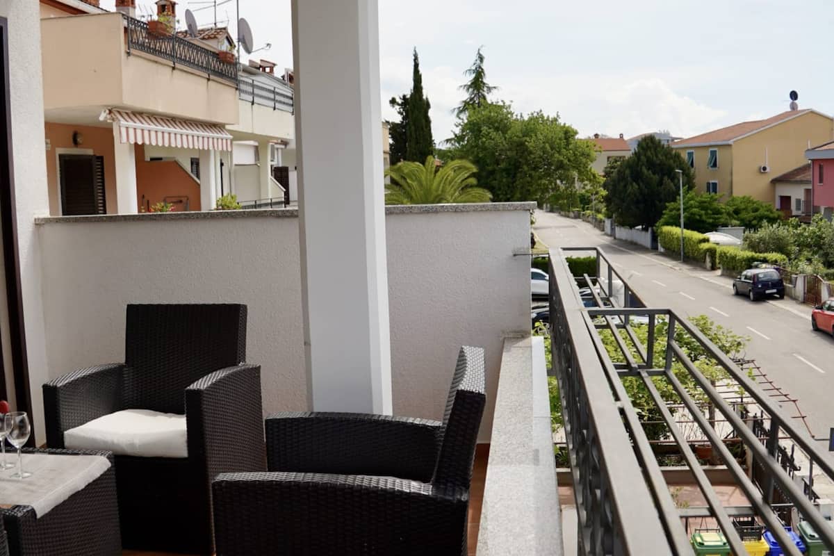 Un balcon doté de meubles en osier et offrant une vue sur une rue résidentielle.