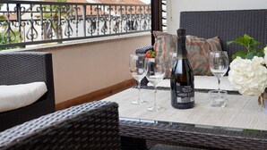 Ein Balkon mit Korbmöbeln, einer Flasche Valdo Extra Dry Wein und zwei Gläsern.