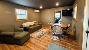 Une pièce avec un plancher en bois, un canapé vert, une table à manger avec des chaises et un téléviseur fixé au mur.