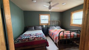 Une chambre avec deux lits, un ventilateur de plafond et des fenêtres.