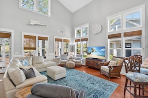 A spacious living room with a large TV, comfortable seating, and a view of the outdoors. - Luxury Golf Front Home with 2 Golf Carts (Miramar Beach)