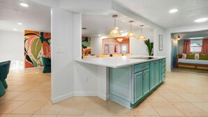 Een moderne keuken met een wit kookeiland, blauwgroene kasten en hanglampen.