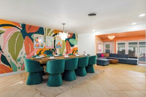 A dining area with a large table and teal chairs, a colorful abstract wall, and a modern sofa in the adjacent living area.