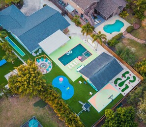 An aerial view of a residential property with a swimming pool, a tennis court, and a landscaped garden.