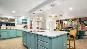 Een keuken met blauwgroene kastjes, een wit eiland en hanglampen.