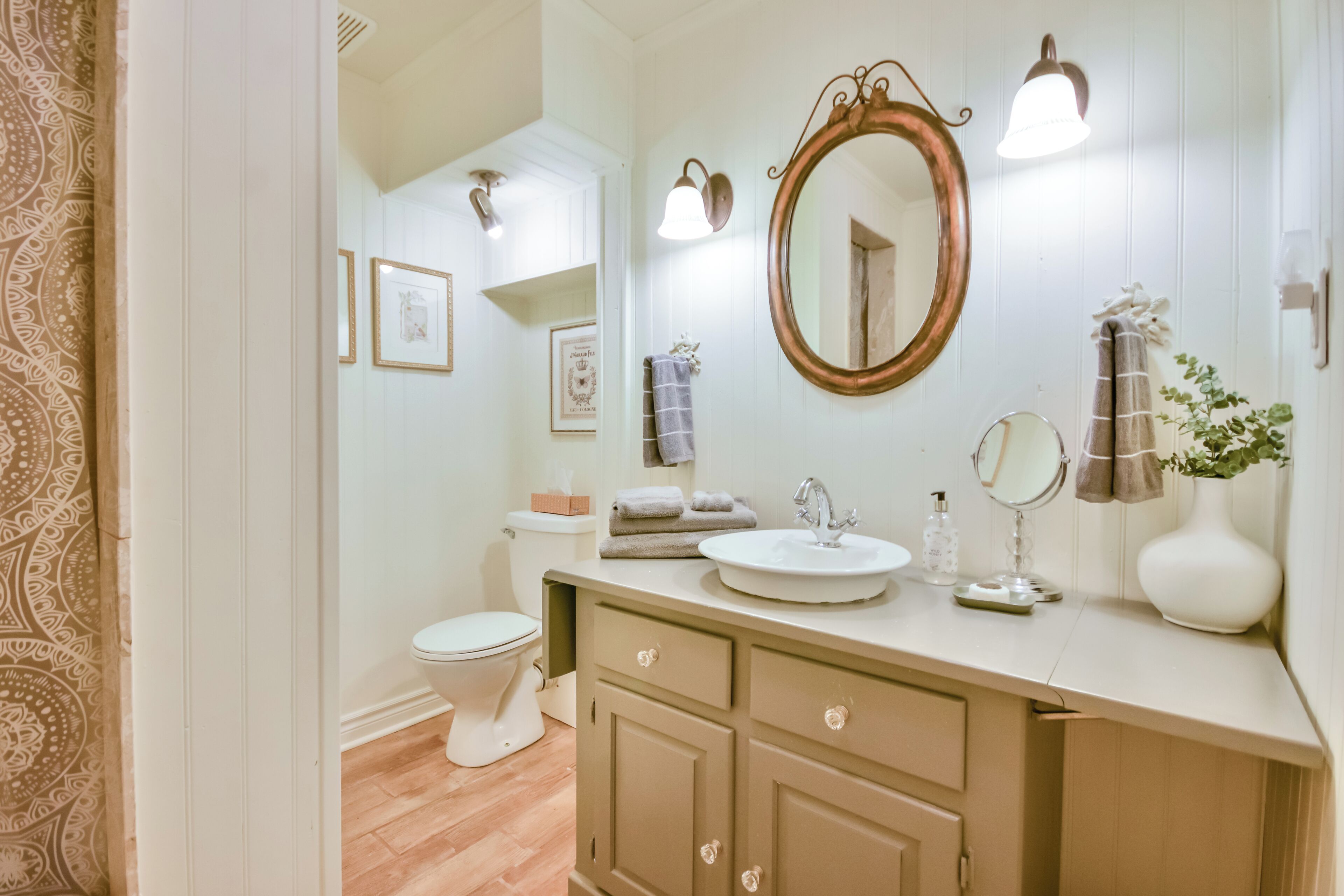 A bathroom with a white sink, vanity, and a large mirror. There are framed pictures on the wall and a towel rack.
