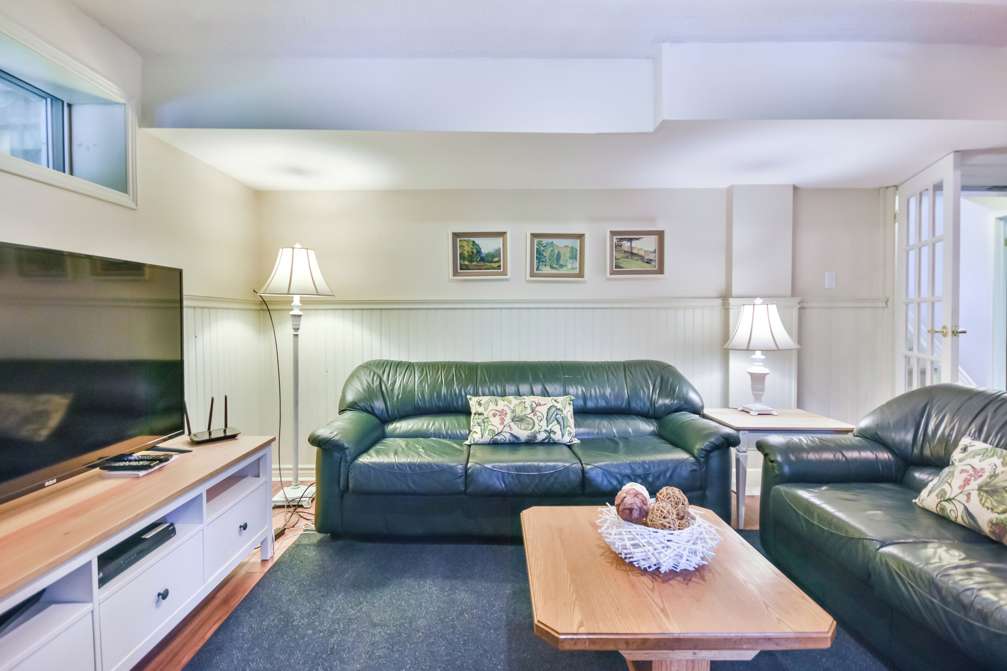 A living room with a green leather sofa, a wooden coffee table, and a flat-screen TV on a wooden stand.