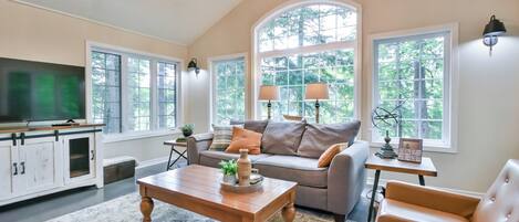 A spacious living room with a large window, a sofa, a coffee table, and a television.