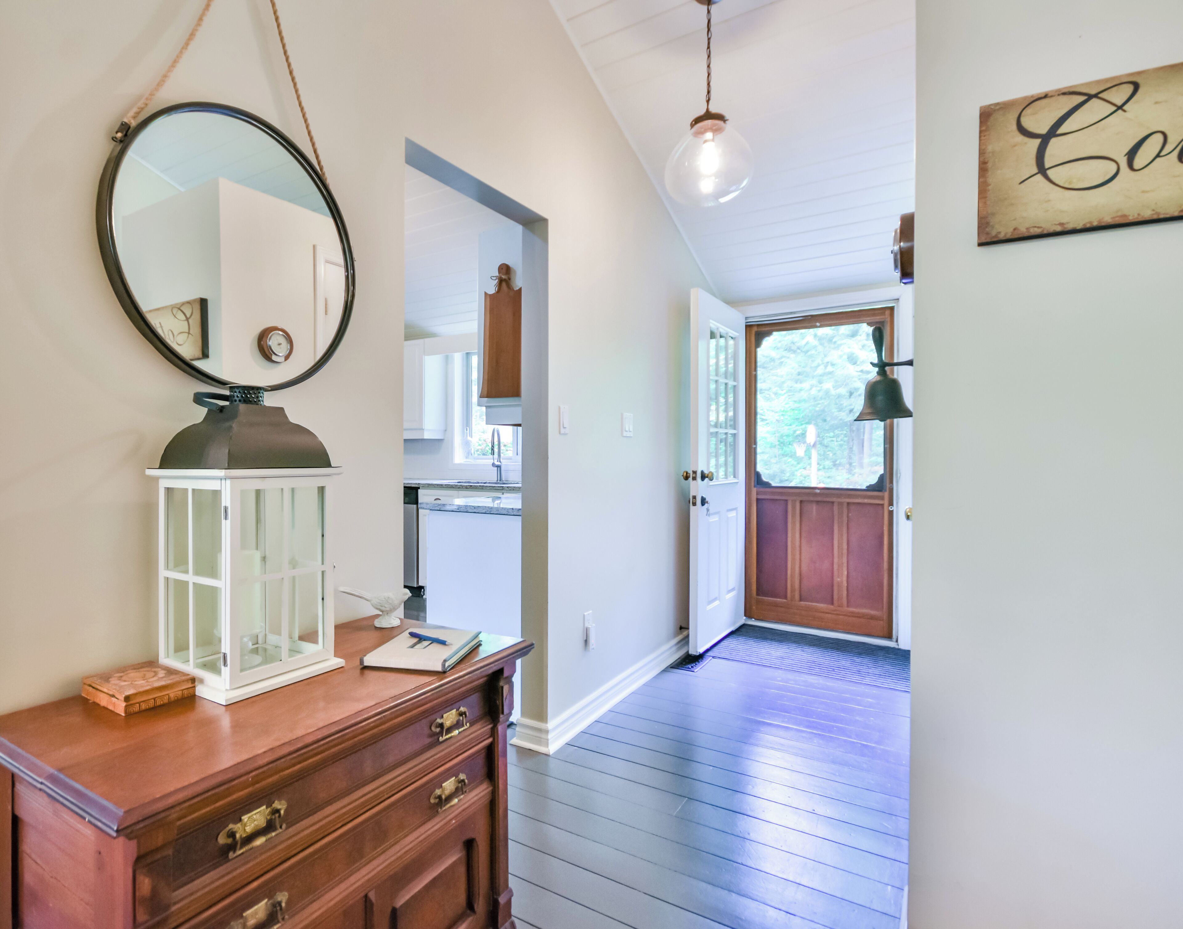 A hallway with a wooden dresser, a mirror, and a door leading to a kitchen.