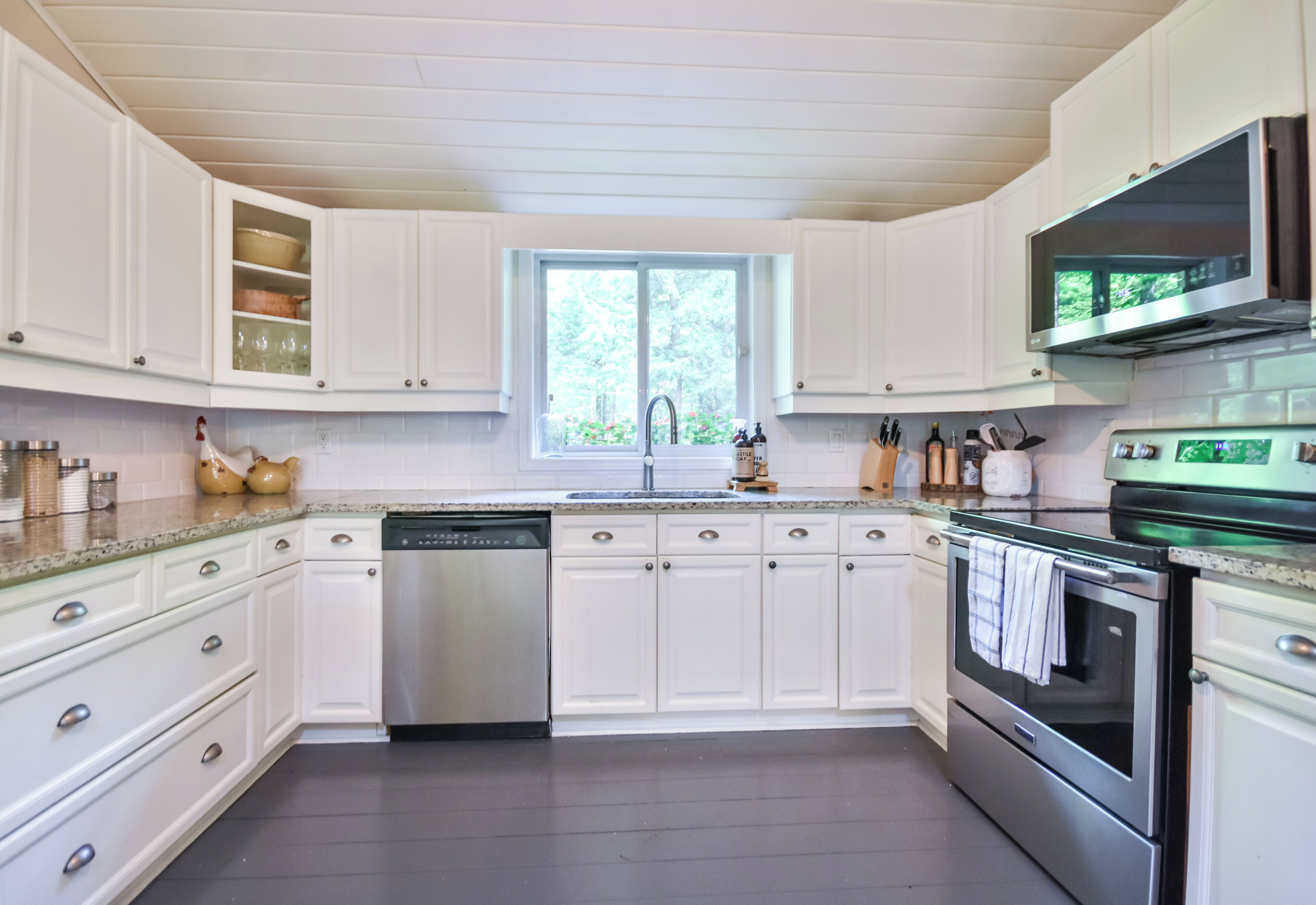 A modern kitchen with white cabinetry, stainless steel appliances, and a window providing natural light.