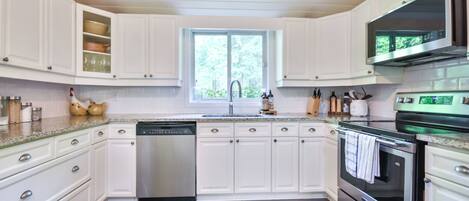 A modern kitchen with white cabinetry, stainless steel appliances, and a window providing natural light.
