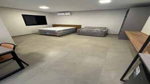 Quarto pequeno e moderno com duas camas, uma escrivaninha, uma cadeira e ar condicionado fixado na parede.
