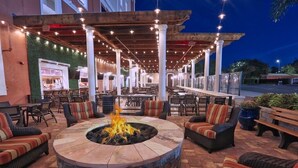 An outdoor seating area with a stone fire pit, cushioned seating, and string lights.