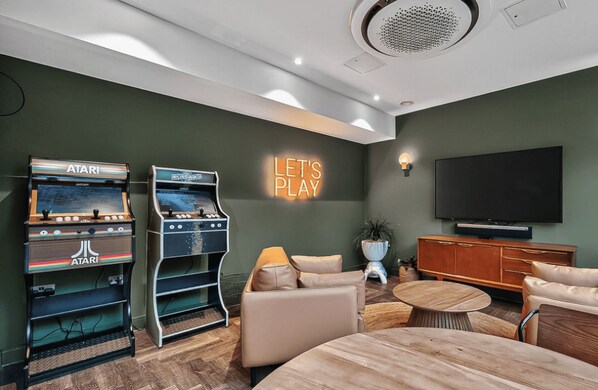 Un salon moderne avec deux bornes d’arcade, un canapé, une table basse et un téléviseur fixé au mur.