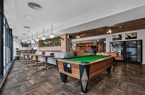 Une table de billard dans un décor intérieur moderne, avec un plancher en bois et des luminaires suspendus.