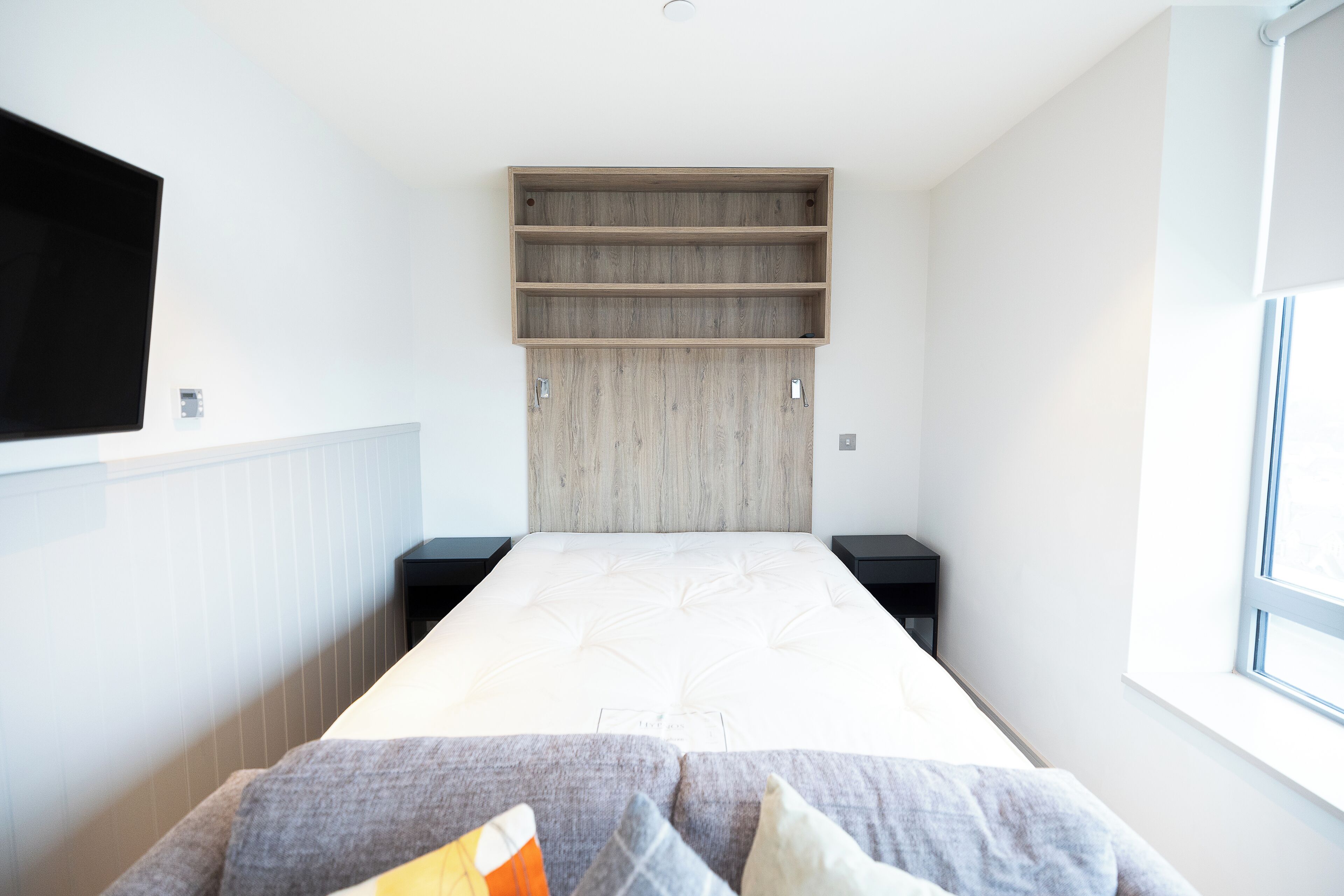 Une chambre à coucher moderne avec un lit, un téléviseur fixé au mur et une fenêtre.