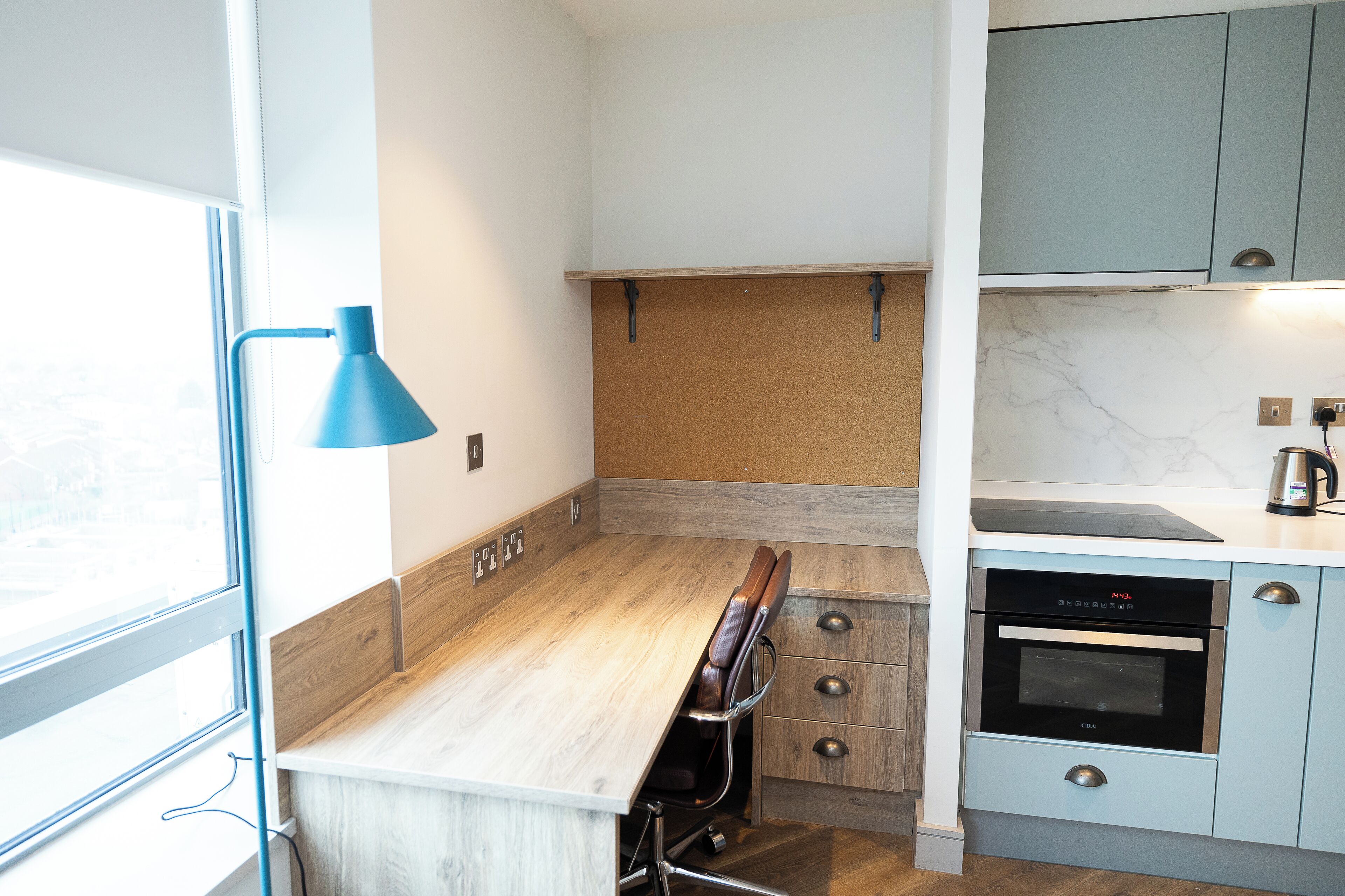 Una cocina con encimera de madera, una lámpara colgante azul, pared de corcho y horno empotrado.