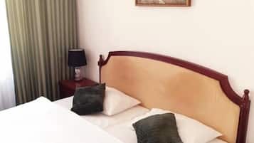 Una cama con sábanas blancas y dos almohadas, una mesita de noche con una lámpara, una cortina verde a rayas y un cuadro en la pared.