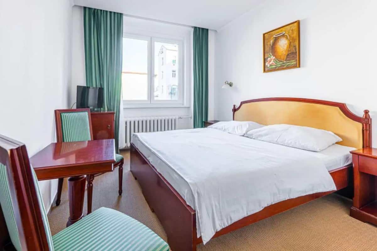 Een hotelkamer met een bed, een bureau, een stoel, een televisietoestel en een raam met gordijnen.