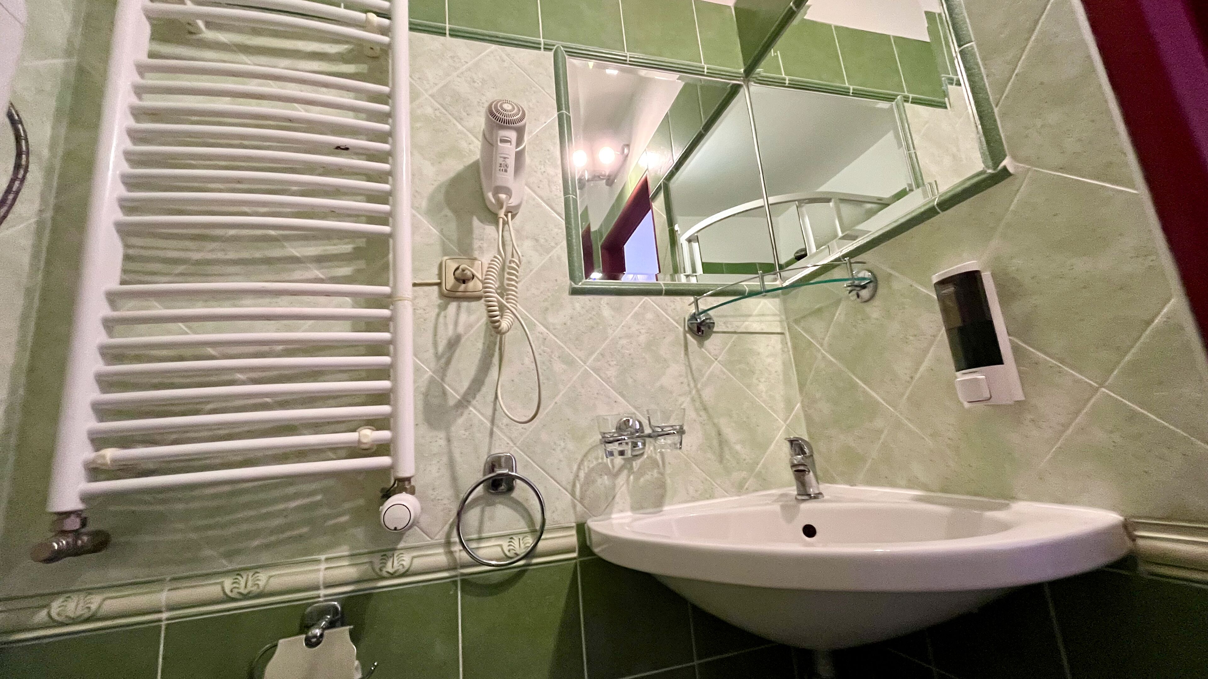 Un bagno con un lavandino bianco, uno specchio, un portasciugamani e un asciugacapelli.