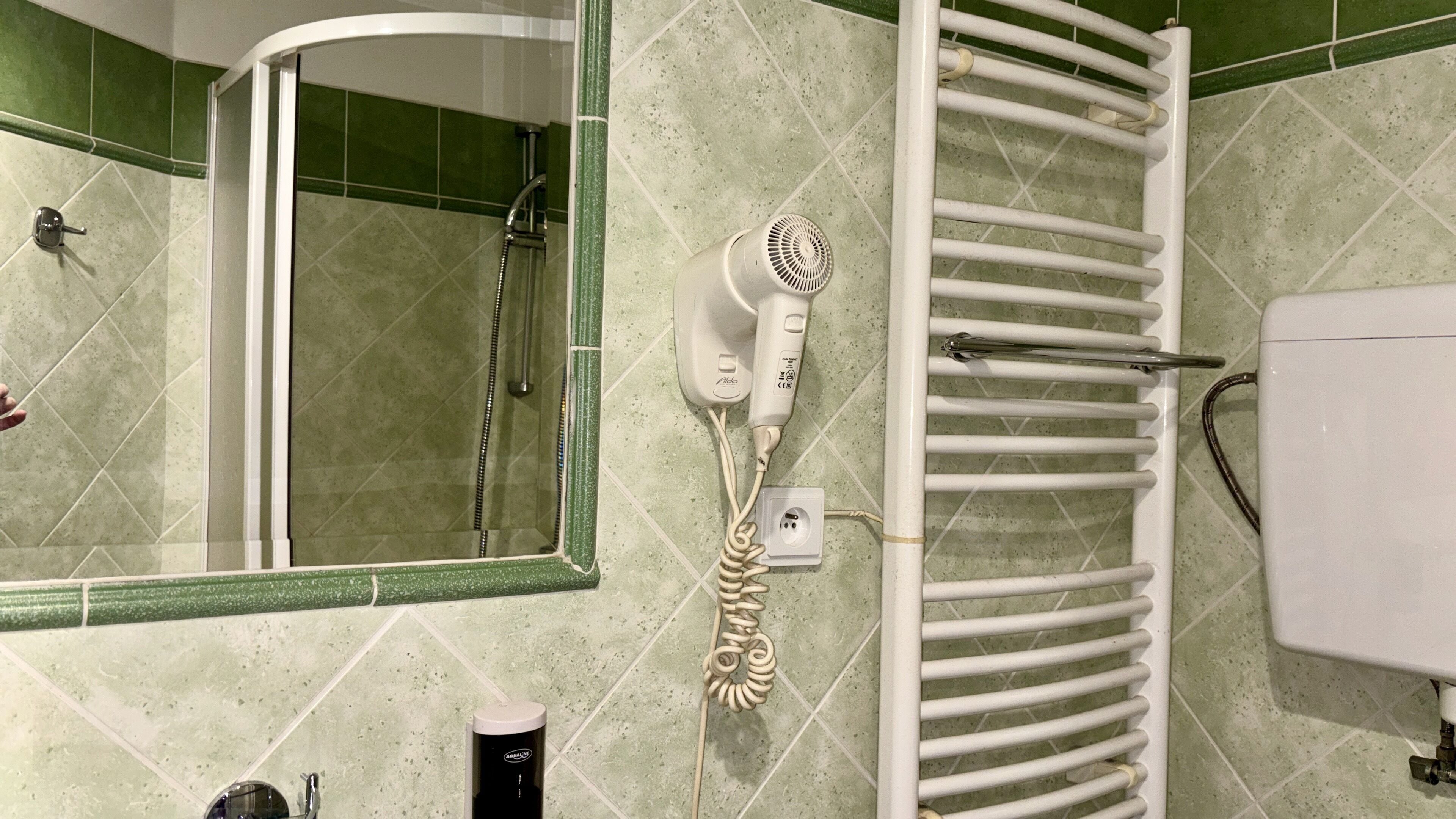 Ein Badezimmer mit Dusche, Fön, Handtuchhalter und Spiegel.