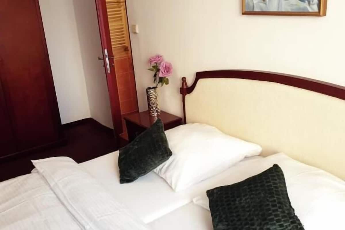Een hotelkamer met een bed, kussens, een schilderij, een vaas met bloemen en een houten deur.