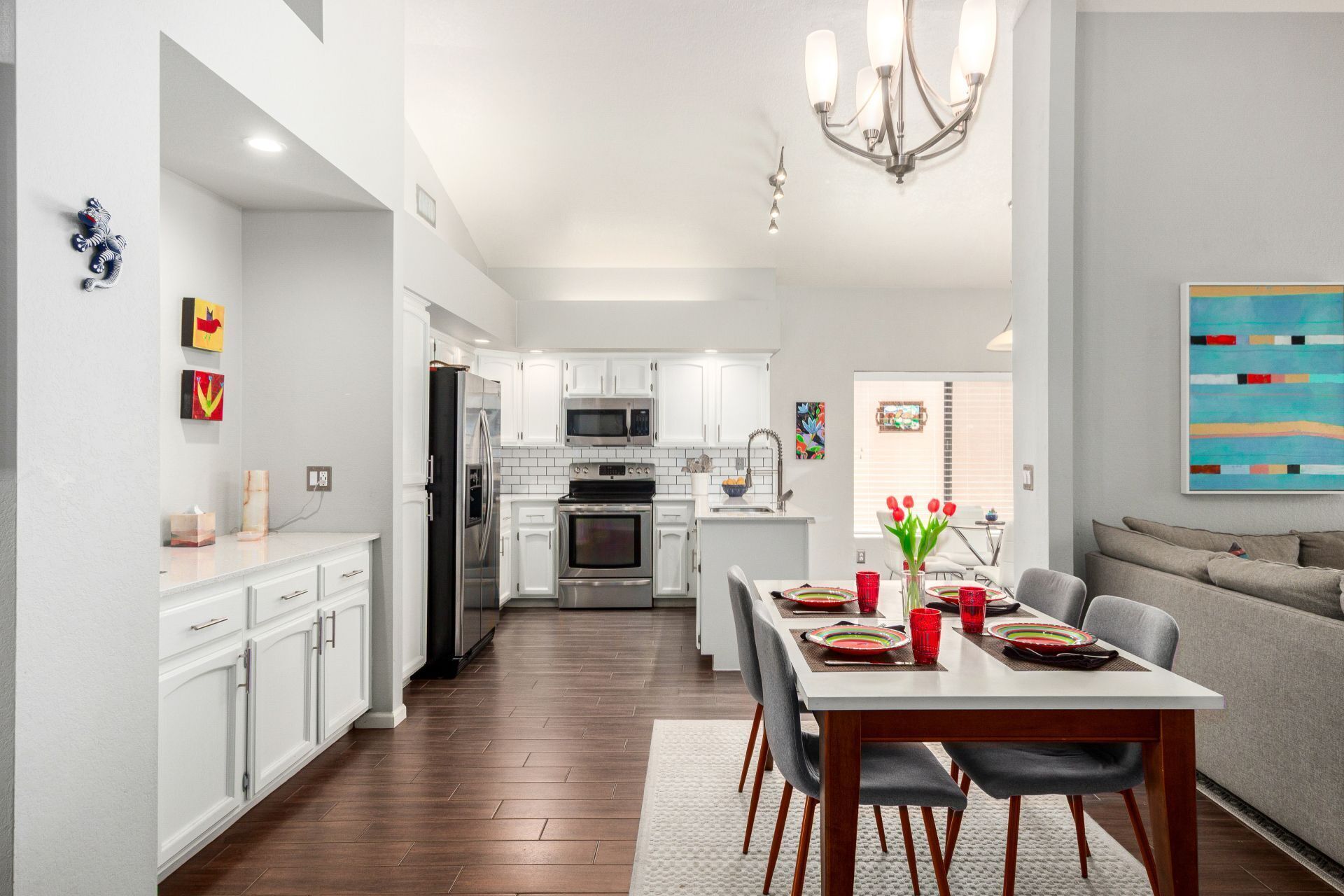 A modern kitchen with white cabinets, a dining area with a table set for four, and a living area with a sofa.