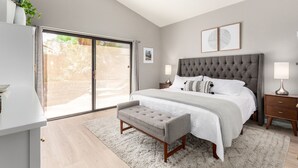 A bedroom with a large bed, a bench, a nightstand, a lamp, and a view through a sliding door. - Cool & Comfy Tucson Summer Retreat w/ Yard (Tucson)