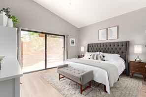 Ein Schlafzimmer mit einem großen Bett, einer Bank, einem Nachttisch, einer Lampe und Blick durch eine Schiebetür.