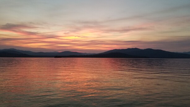 Un lago tranquilo al atardecer con montañas al fondo.