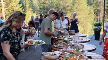 A group of people dining outdoors at a wooden table with various dishes.