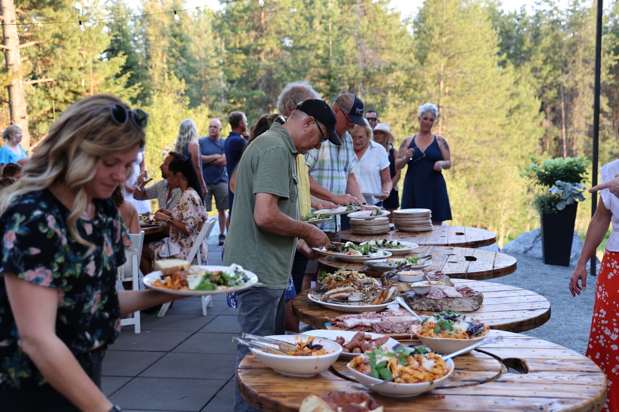A group of people dining outdoors at a wooden table with various dishes.