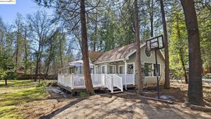 Une maison de plain-pied avec un porche, entourée d’arbres.