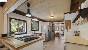 Une cuisine moderne dotée d’un îlot central, d’un plafond en bois et de grandes fenêtres.