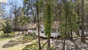 Une maison à deux étages avec un porche, entourée d’arbres.