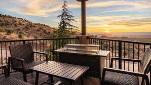 Une terrasse avec une table et des chaises, offrant une vue sur un paysage désertique, avec un arbre et des montagnes en arrière-plan.