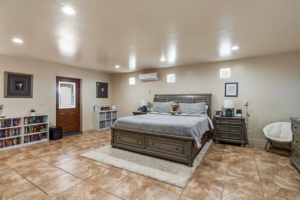 A bedroom with a large bed, a bookshelf, a door, and a white chair.