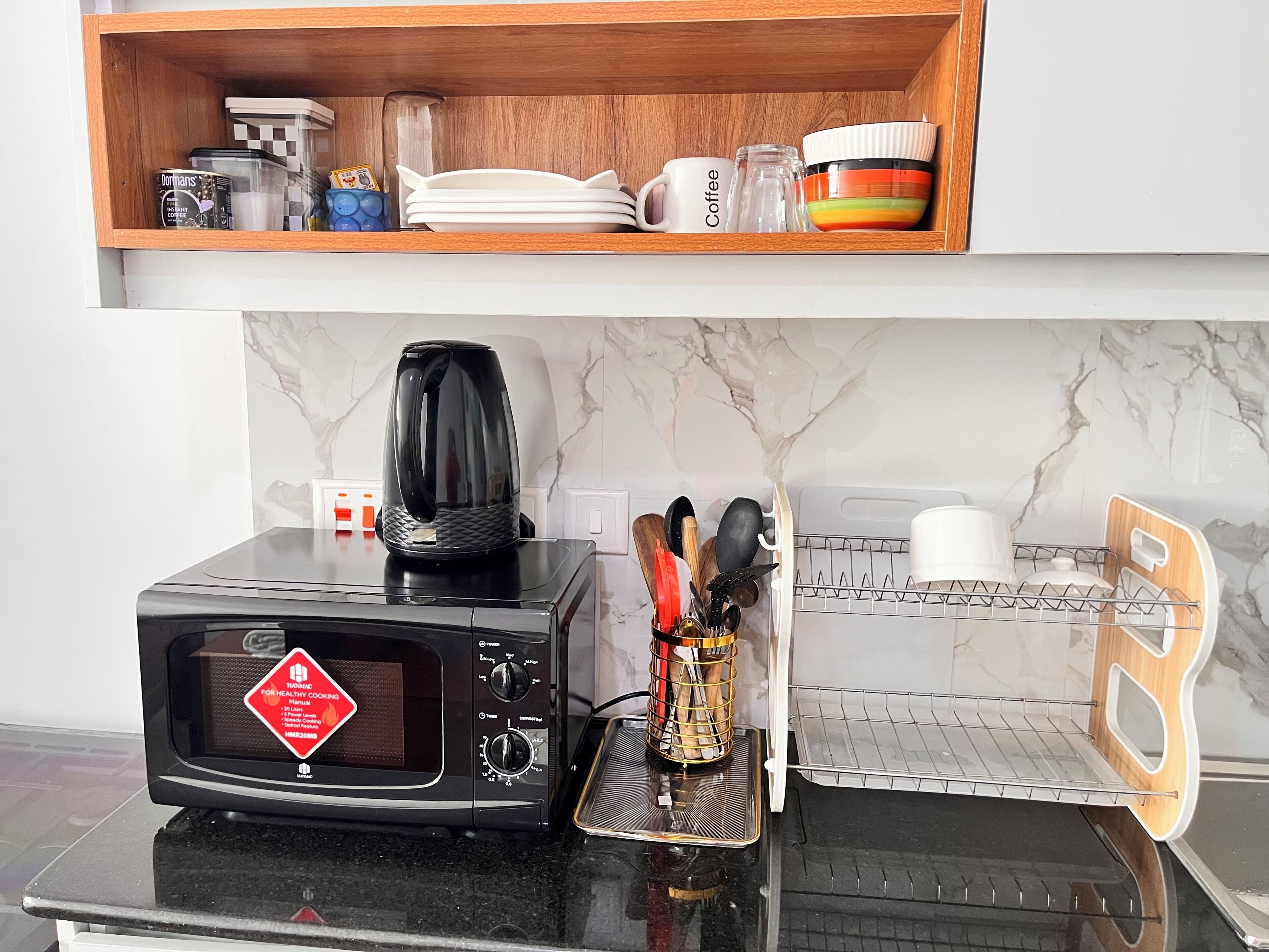 Una cucina con forno a microonde, macchina del caffè e utensili sul piano di lavoro.