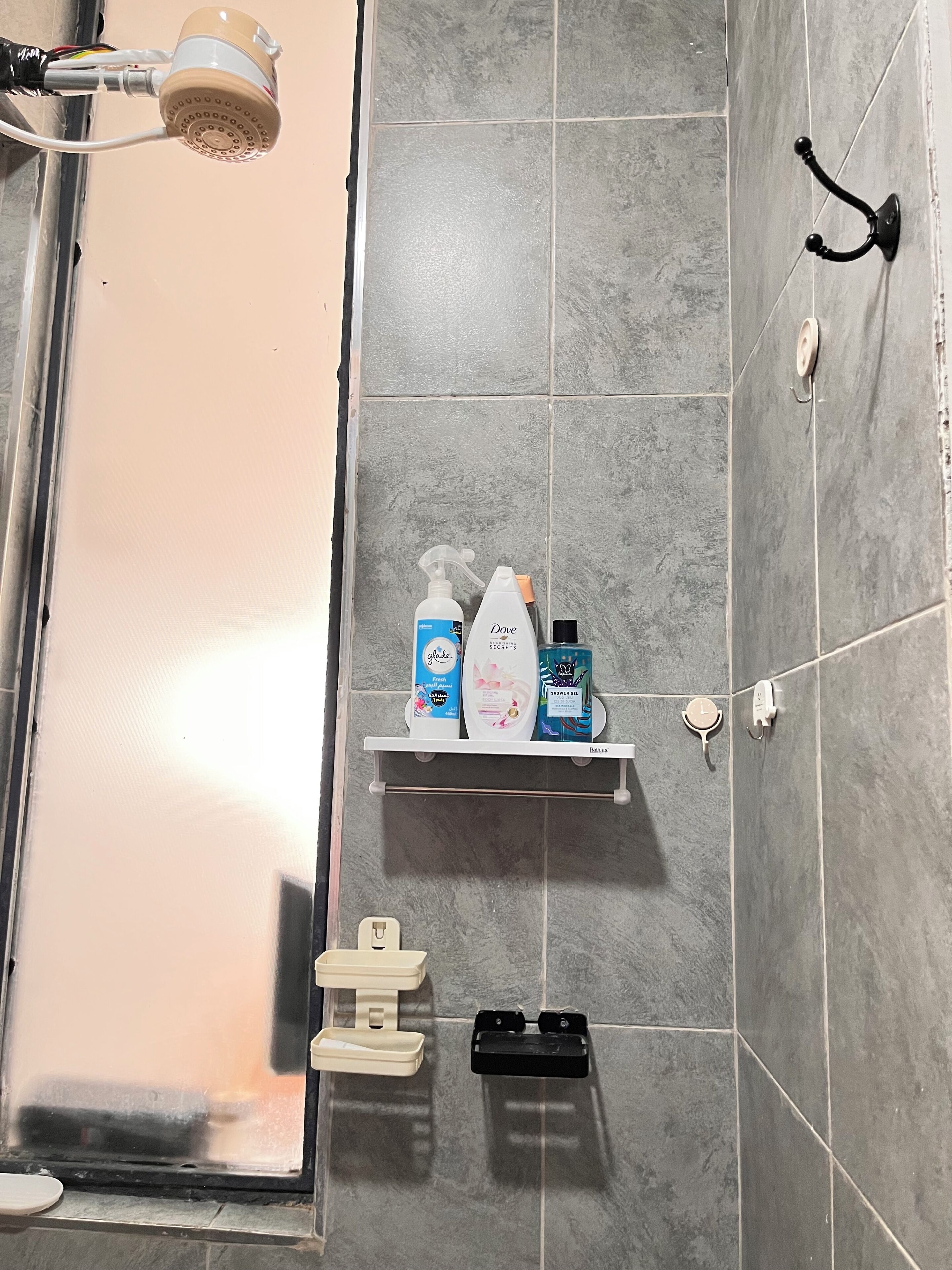 Un baño con ducha, un estante de artículos de aseo y un perchero.