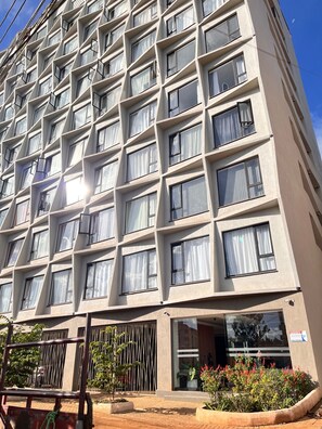 Un hotel de varios pisos con fachada geométrica, ventanas amplias y entrada protegida por un portón.
