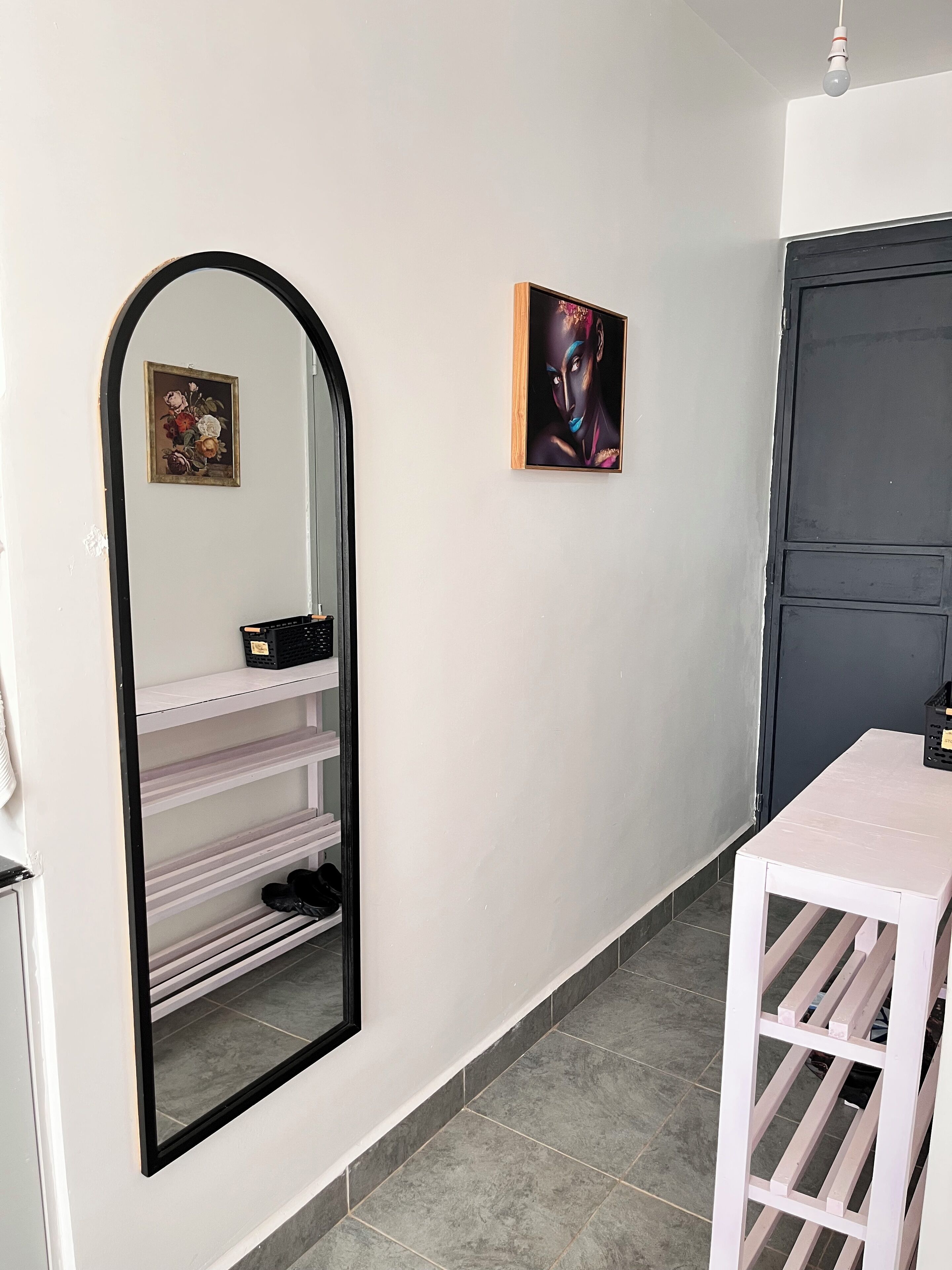 Un couloir avec un miroir, une étagère à chaussures, une petite table et une porte.