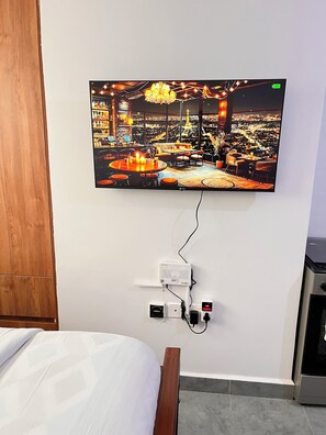 Ein an der Wand befestigter Flachbildfernseher zeigt eine Restaurantszene mit Tischen, Stühlen und Blick auf die Stadt.