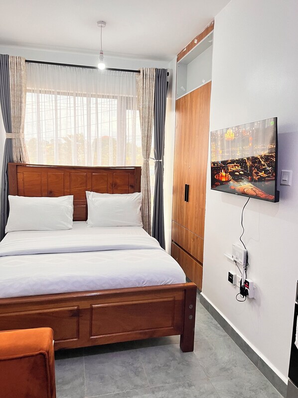 Ein ordentlich eingerichtetes Schlafzimmer mit einem Holzbett, einem flachbildfernseher an der Wand und einer sichtbaren Steckdose.