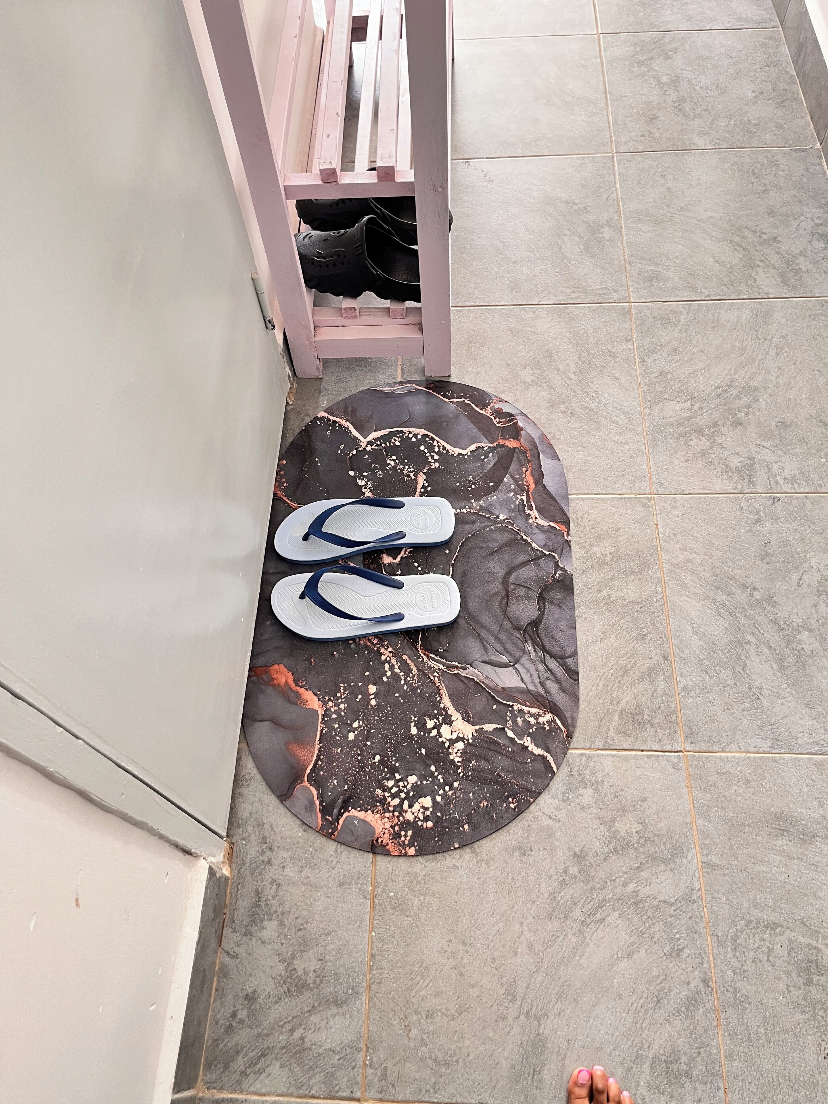 A pair of flip-flops on a dark, marbled mat near a white door with a pink frame.