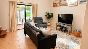 A spacious living room with a ceiling fan, a sofa, a TV, and a large window with curtains.