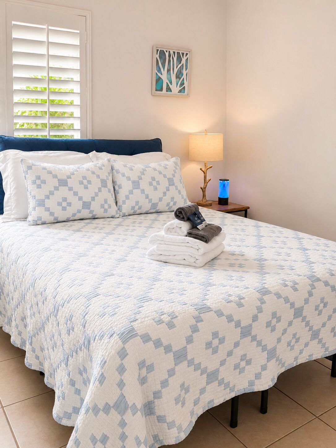 Een net opgemaakt bed met een bedsprei met een patroon, een kussen en een opgevouwen handdoek op het bed.