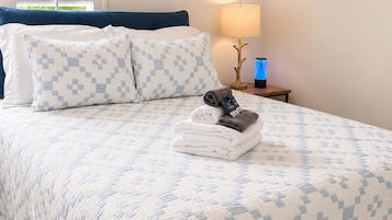 Een net opgemaakt bed met een bedsprei met een patroon, een kussen en een opgevouwen handdoek op het bed.