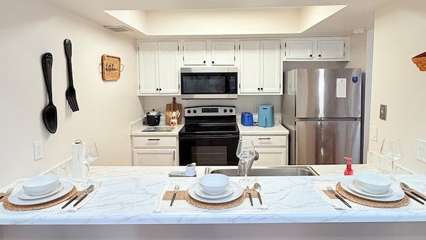 A modern kitchen with white cabinets, a stainless steel refrigerator, and a dining area with a marble countertop and brown chairs.