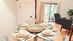 A dining area with a glass table set for four, surrounded by four grey chairs.