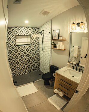A bathroom with a patterned wall, a toilet, a sink with a mirror, and a shower area. - Casita Verde 2-br guest house under an oak canopy, ideal spot in Palm Beach G... (Palm Beach Gardens)